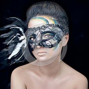 Mysterious beautiful girl in a black mask with feathers with green creative makeup in the studio on a dark background isolated