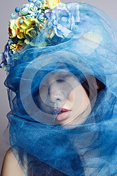 Mysterious beautiful woman with floral hat, female with makeup, hiding her face with blue veil.