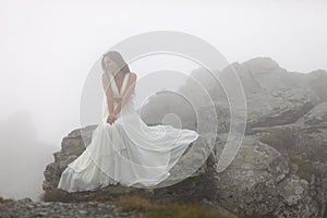 Mysterious bride sitting on rocky mountain top
