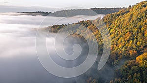 Mysterious fog rising over a valley with a colorful autumn forest at sunrise