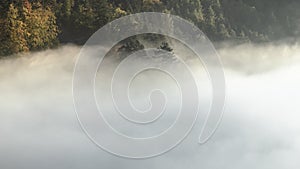 Mysterious fog rising over a valley with a colorful autumn forest at sunrise