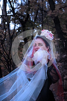 A mysterious Gothic woman in a long black Victorian dress and a white veil with blood. Halloween concept. A classic horror scene.