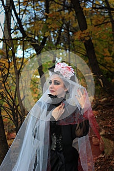 A mysterious Gothic woman in a long black Victorian dress and a white veil with blood, holds a bird. Halloween concept. A classic