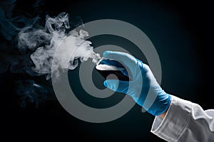 Mysterious hand holds vial releasing vapor in blue glove on dark background photo