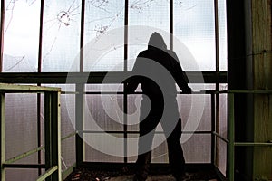 A mysterious hooded, figure, back to camera, standing in a abandoned industrial building