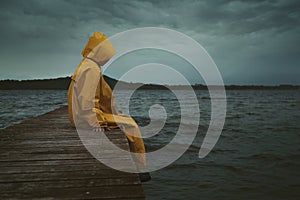 Mysterious hooded figure seated on a pier