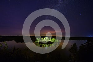 Mysterious illuminated island on the forest lake at night