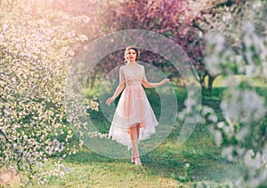 Mysterious lady with dark gathered hair in a light delicate peach dress walks in the blooming garden, the spring fairy