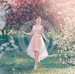 Mysterious lady with dark gathered hair in a light delicate peach dress walks in the blooming garden, the spring fairy