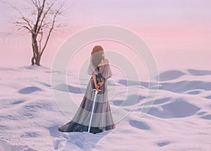 Mysterious lady from Middle Ages with dark hair in gentle gray blue dress in snowy desert with open back and shoulders