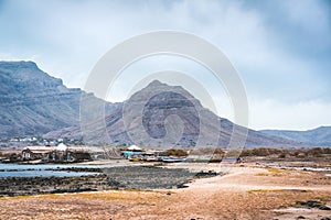 Mysterious landscape of sandy coastline with fisher village and black volcanic mountains in background. Baia Das Gatas