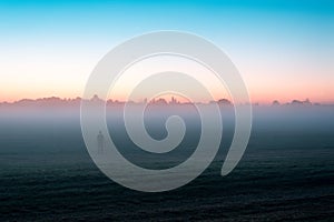 A mysterious lone ghostly, figure standing in a field just before sunrise. On a misty summers morning.