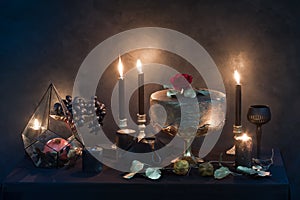 Mysterious looking still life with handmade figure of cake, burning candles, dried rose and pomegranate