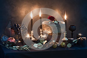 Mysterious looking still life with handmade figure of cake, burning candles, dried rose and pomegranate in a prism