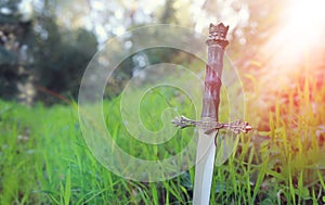 mysterious and magical photo of silver sword over England woods or field landscape with light flare. Medieval period concept.
