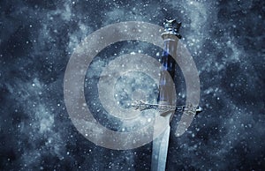 mysterious and magical photo of silver sword over gothic snowy black background. Medieval period concept.