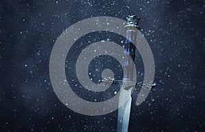 mysterious and magical photo of silver sword over gothic snowy black background. Medieval period concept.