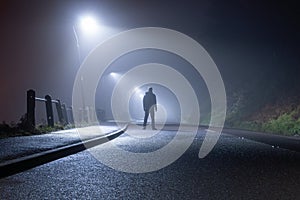 A mysterious man, alone, standing in the middle of a country road. Under street lights. On a foggy, moody, spooky, winters night