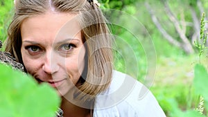 A mysterious middle-aged beautiful woman peeks out from behind a tree trunk.