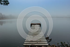 Mysterious morning by lake. Foggy autumn mystery atmosphere. Wooden pier on the pond.Magic mood. Misty fall day. Speechless place