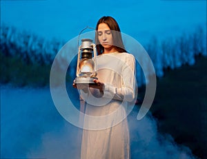 Mysterious mystical girl in a dark night forest with a kerosene lamp in her hands