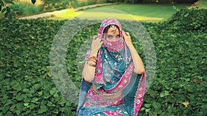 Mysterious oriental beauty fantasy woman sitting in tropical garden, green ivy. India princess covers face national blue