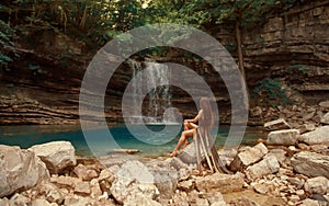 Mysterious river nymph on bare rocks near small blue lake in Martvili Canyon Lagoon and wonderful waterfall, girl with