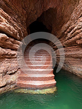 Mysterious underground cave with stairs leading to emerald green water photo