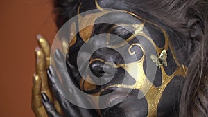 Mysterious woman in black and gold body art posing on camera, close up