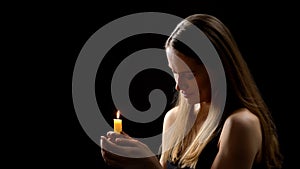 Mysterious woman holding candle in hands and praying with closed eyes, rituals