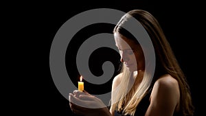 Mysterious woman holding candle in hands and praying with closed eyes, rituals photo