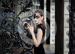 Mysterious woman in venetian carnival mask near wrought iron gate