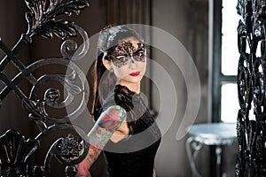 Mysterious woman in venetian carnival mask near wrought iron gate