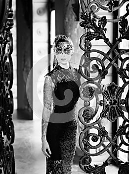 Mysterious woman in venetian carnival mask near wrought iron gate. Noir style