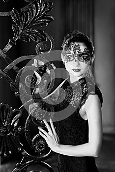 Mysterious woman in venetian carnival mask near wrought iron gate. Noir style