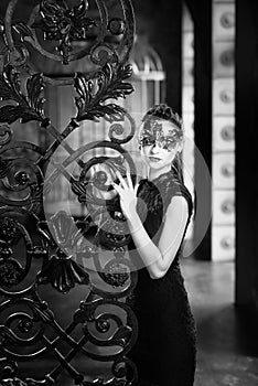 Mysterious woman in venetian carnival mask near wrought iron gate. Noir style