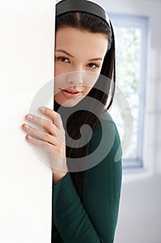 Mysterious young female hiding behind wall