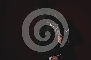 Mysterious young man in tuxedo fixing collar on black background