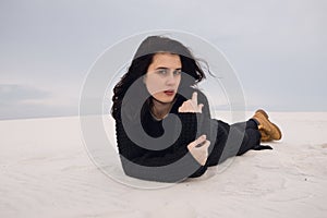Mystery girl in black lies on the dune in the desert