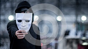 Mystery hoodie man with black mask holding white mask in his hand. Anonymous social masking or bipolar disorder concept