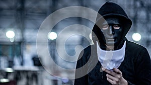 Mystery hoodie man with broken black mask holding white mask in his hand. Anonymous social masking or bipolar disorder concept