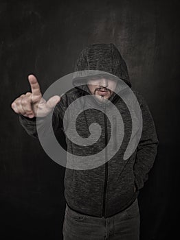 Mystery unknown man in hood pointing by finger on dark