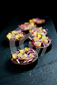 Mystic dark chocolate pralines with candied orange and red knapweed petals on dark background