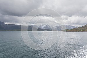 A mystical fjord in Norway with mountains and fog hanging over the water in polar day. midnight sun, selective focus