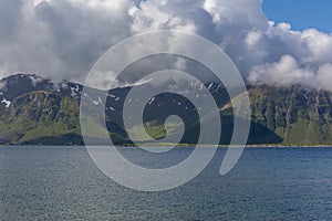 A mystical fjord in Norway with mountains and fog hanging over the water in polar day. midnight sun, selective focus