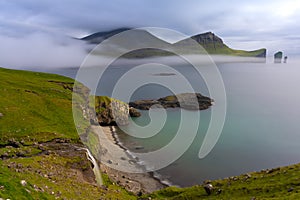 Mystical foggy lansdcapes along the coast of Vagar Island, Faroe Islands with the SkarÃ°sÃ¡fossur waterfall in the foreground