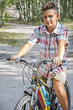 N the summer, in the forest, a boy rides a bike on the road.