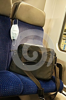 A N95 face mask or nose mouth protection mask on a seat in an empty commuter train with a business bag showing the mask is a perso