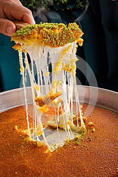 Nabulsiyeh dessert with someone taking a piece of it and spreading the cheese