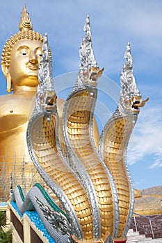 Naga and large gold buddha statue under construction in Thai temple with clear sky.WAT MUANG, Ang Thong, THAILAND.